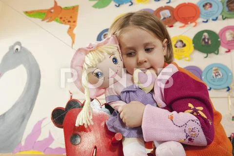 Germany, Girl (3-4) sitting on rocking horse, holding doll, portrait Stock Photos