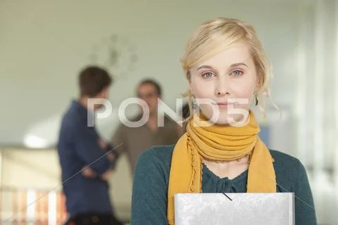 Germany, Leipzig, Young woman holding book with students standing in background Stock-Fotos