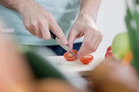 Germany, Mid section of man cutting tomato, close up Stock Photos