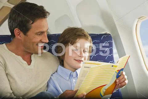 Germany, Munich, Bavaria, Man and boy reading book in economy class airliner Stock Photos
