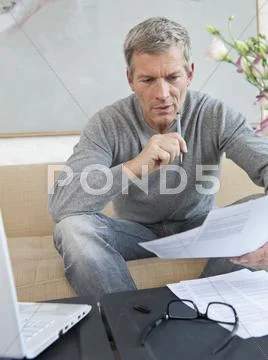 Germany, Munich, Mature Man Doing Paperwork With Laptop