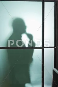 Germany, Munich, Silhouette of businessman behind frosted glass, hand to chin Stock Photos