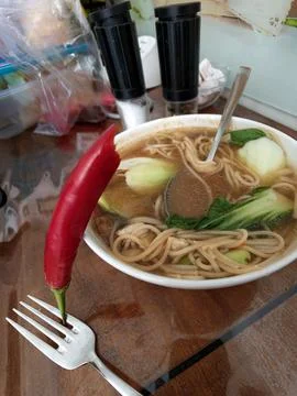 Germany red chili pepper on fork near noodle soup with bok choy on wooden tab Stock Photos