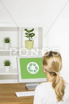 Germany, Woman sitting at computer, rear view, Recycling symbol on screen Stock Photos