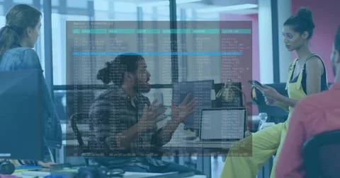 Gesturing man explaining in open office, woman in yellow holding phone, screens 库存照片