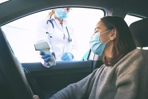 Get checked and get going. a masked young woman getting her temperature checked Stock Photos