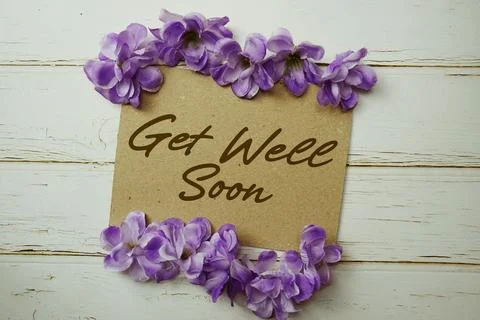 Get Well Soon text written on paper card with flower decoration on wooden b.. Stock Photos