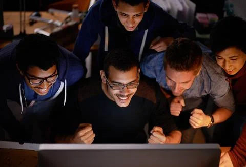 Getting behind the team. a group of young man cheering at a monitor in a dark Foto stock