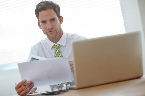 Getting the contracts in order. A young businessman looking at a document while Stock Photos