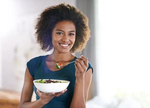 Getting her greens. Portrait of an attractive young woman eating a bowl of salad Stock Photos