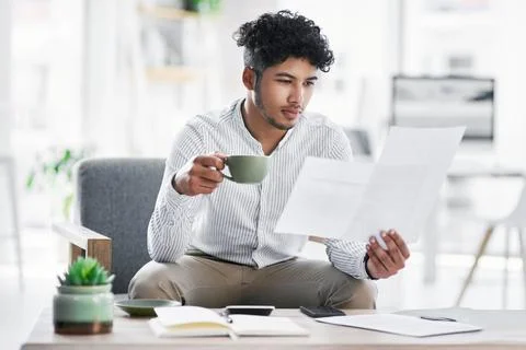 Getting his admin up to date. a young businessman drinking coffee while going Stock-Fotos