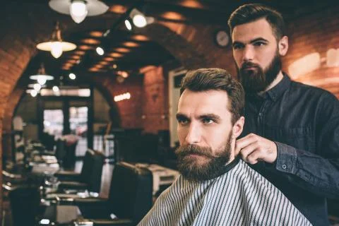 Getting ready to cut the beard. Guy is sitting in chair withcovered shoulders Foto stock