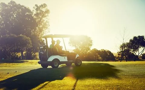 Getting into the swing of things. two golfers riding in a cart on a golf course. Stock Photos