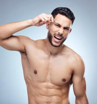 Getting those brows in shape. Shot of a young man tweezing his eyebrows against Stock Photos