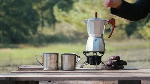 A geyser coffee maker stands on the burner along with cups and treats against 库存影片 123468005