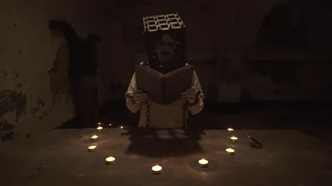 Ghost with cage on his head reading spells next to crucified body in basement. Stock Footage 245576994