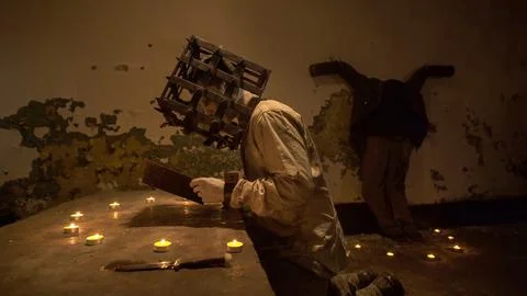 Ghost with cage on his head reading spells next to crucified body in basement Stock Photos