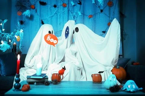 Ghost couple having Halloween fun at home with a Boo sign. Enjoying a party.. Stock Photos
