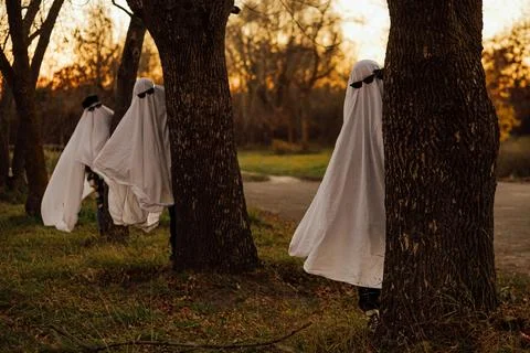 Ghost figures hiding behind trees in forest at sunset Stock Photos