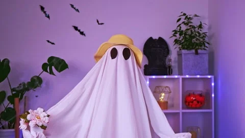 A ghost gardener in a straw hat sniffs flowers. Halloween concept. Funny ghost Stock Footage 218613816