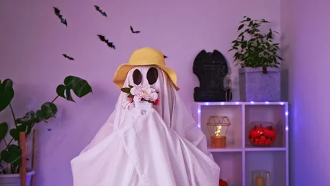 A ghost gardener in a straw hat sniffs flowers. Halloween concept. Funny ghost Stock Footage 233011256