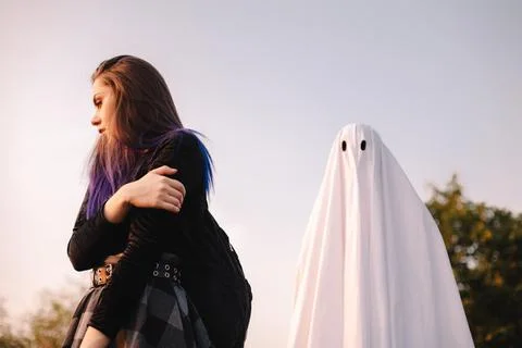 Ghost standing behind scared young woman outdoors during Halloween Stock Photos