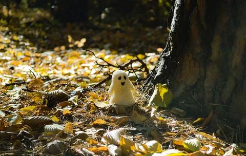 A ghost toy stands next to a tree trunk among the leaves in the autumn forest Foto stock