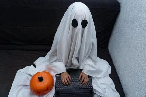 Ghost working from home on his computer sitting on the couch with a pumpkin Stock Photos