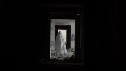 Ghostly figure in sheet stands framed by doorway in run-down, graffiti-covered Stock Footage 320246474