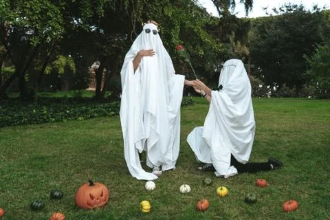Ghosts couple giving rose while kneeling surrounded by pumpkins Foto stock