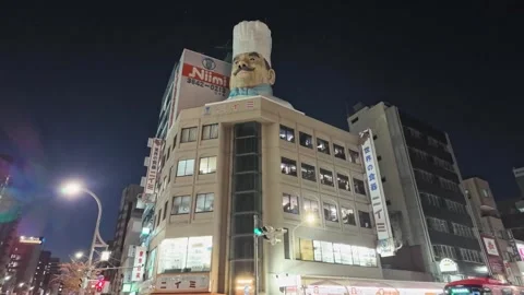 A giant chef head stands atop a building while a red bus passes by. Vídeos de archivo 346012602