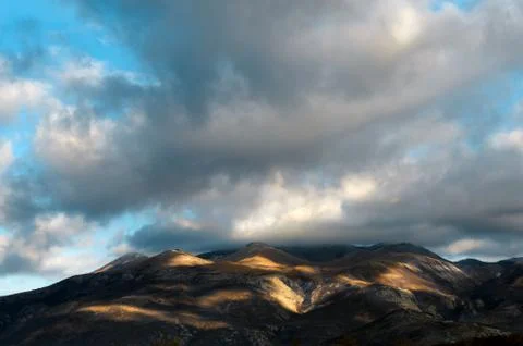 Giant clouds scattering shadows over a hill below with autum colors Stock Photos