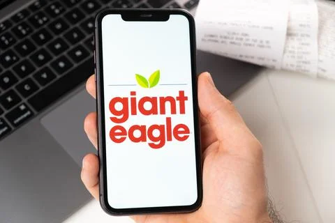 Giant eagle application on the screen of Apple iPhone in mans hand and laptop on Stock Photos