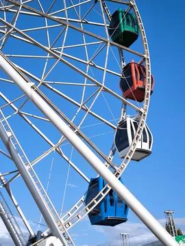 A giant Ferris wheel with multi-colored enclosed cabins against a clear sky. Stock Photos