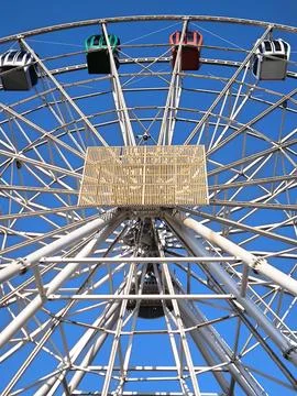 A giant Ferris wheel with multi-colored enclosed cabins against a clear sky. 스톡 사진