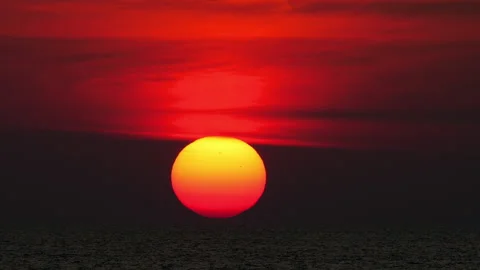 Giant orange sun setting over dark ocean horizon with dramatic red sky Stock Footage 336461814