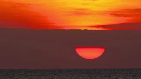 Giant red sun setting behind clouds over calm ocean water Stock Footage 341357371