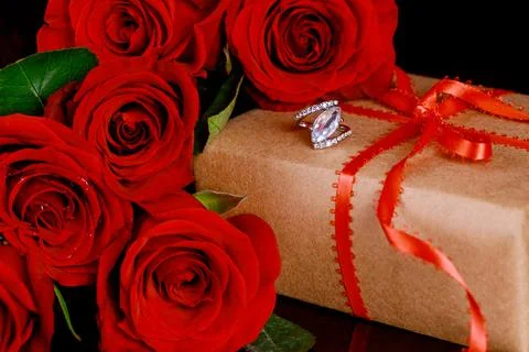 Gift and ring with beautiful red roses on black background. Valentines Day. Stock Photos