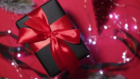 Gift black box with red ribbon on top of christmas tree decorations with bokeh Stock Footage 165865983