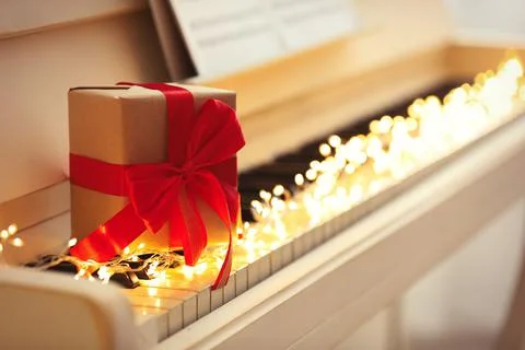 Gift box and fairy lights on piano keys, space for text. Christmas music Stock Photos