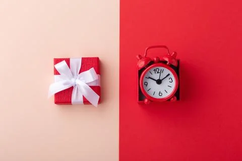 Gift box and red clock on pink and red background, flat lay Stock Photos
