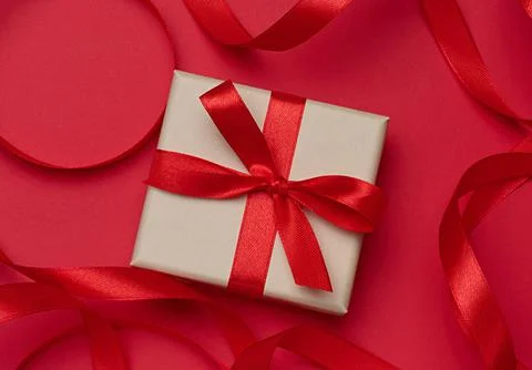 Gift box in beige packaging with red satin bow on a red background Stock Photos