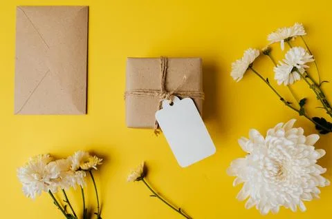 Gift box with blank tag, envelope and flowers is placed on yellow background Stock Photos