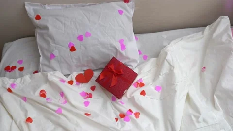 Gift box with a bow and red hearts are flying on the bed. Valentine's day gift Stock Footage 168396749