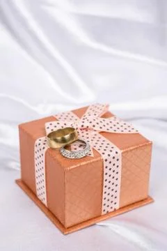 Gift box with bow and wedding rings over white satin Stock Photos
