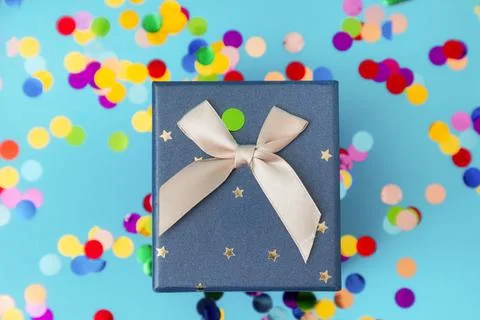 Gift box with a bow on a blue background with colorful confetti. Flat lay. Th Stock Photos