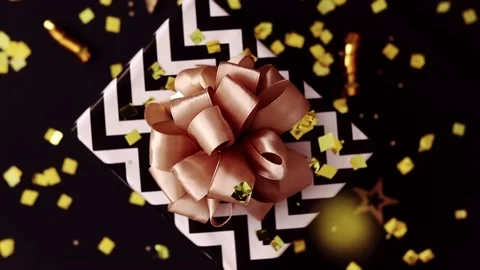 Gift box with a bow rotates on a black background, sparkles of festive confetti Stock Footage 217677851