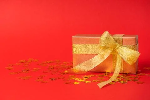 Gift box in a gold wrapper with a gold bow on a starry colored background. Stock-Fotos