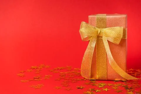 Gift box in a gold wrapper with a gold bow on a starry colored background. Stock Photos