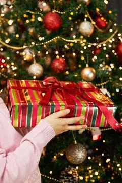 Gift box in hands, wrapped in colored paper and tied with a red ribbon, against Stock Photos
